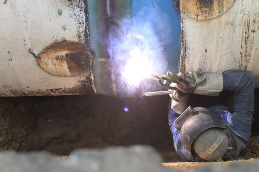 Male welder worker wearing protective clothing fixing welding   and sewerage plumbing pipeline outside on site