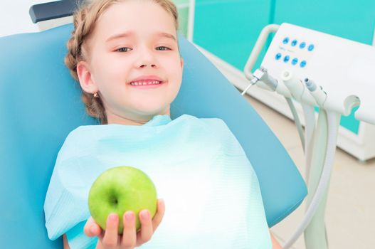 girl in the dentist's chair shows a green apple, regular care of your teeth