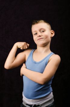 A young boy showing off his muscles on black background
