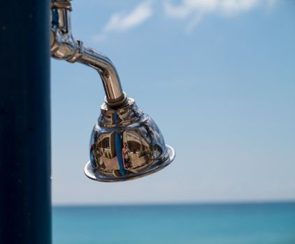 Reflections in a chrome silver shower head by beach with hotel reflected