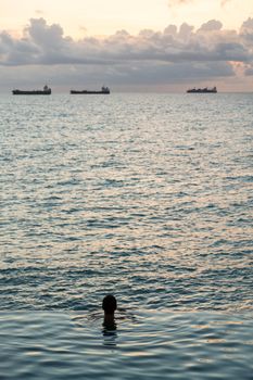 Silhouette of person head at the edge of infinity swimming pool overlooking ocean at sunset