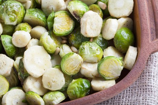 Roasted parsnips and brussel sprouts in terracotta baking dish.
