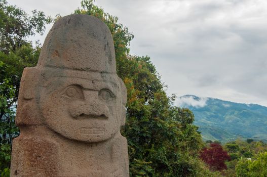 An ancient statue with trees and hills behind it.