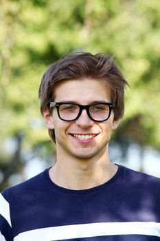 Portrait of young and smiling cute man with glasses in park