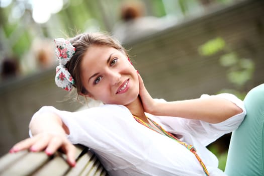 A beautiful woman is sitting on a park bench on a blurred background
