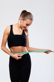 Happy and beautiful girl measuring her waist fitness with a ruler over grey background