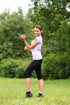 Young woman doing her fitness exercises with red dumbbells in the park