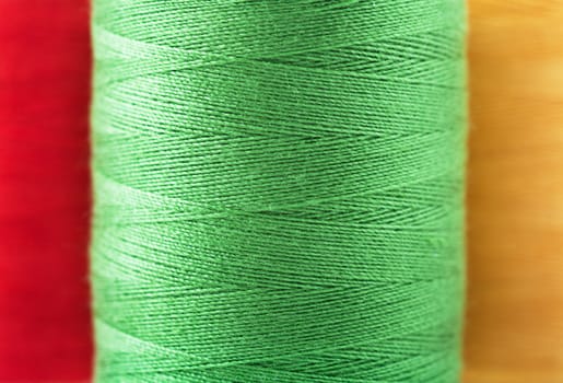 Macro view of reel of green, red and yellow thread spools.