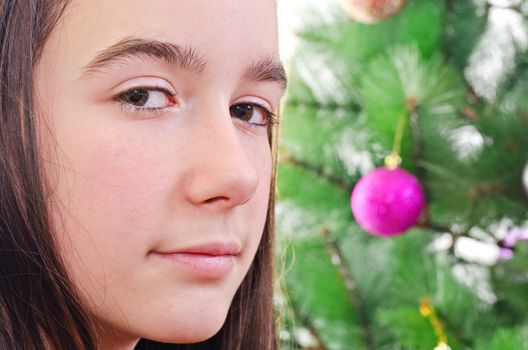 Face closeup with eye contact of young girl, christmas tree in background, horizontal shot