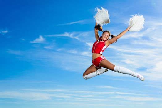 Young cheerleader in red costume jumping against blue sky