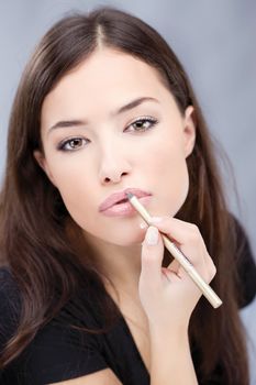 applying cosmetic pencil on woman's lips, focus on lips