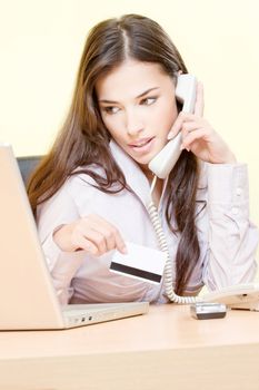 Pretty woman talking over phone, holding credit card and looking at the laptop