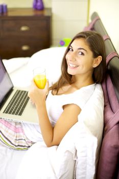Beautiful smiling girl with computer and orange juice in bed