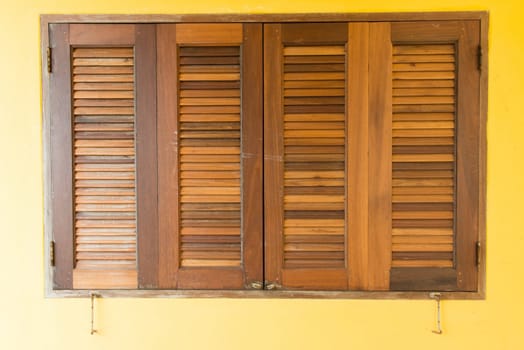 Brown wooden closed windows on yellow concrete wall