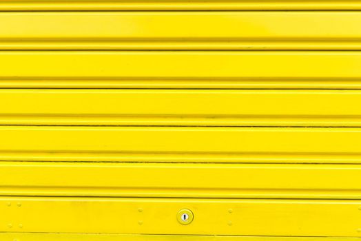 Bright yellow metal sliding door with key hole, taken on a cloudy day.