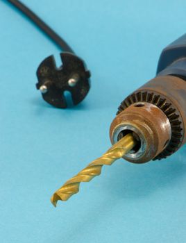 rusty old electric drill with golden bit and rosette plug closeup on blue background.