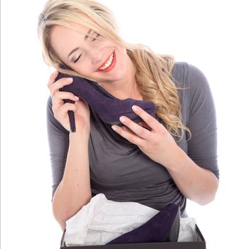 Happy young blonde woman holding purple high heel to her face and smiling on white background Happy woman shopper caressing a newly purchased and unwrapped shoe with her cheek with a look of bliss isolated on white