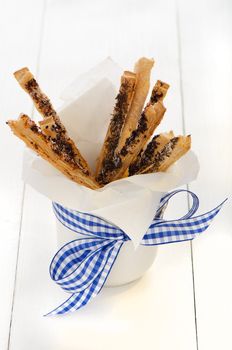 spicy puff pretzel sticks in a white cup with a blue ribbon as decoration on white wooden table