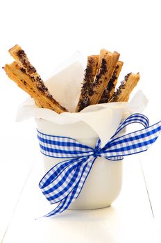 spicy puff pretzel sticks in a white cup with a blue ribbon as decoration on white wooden table
