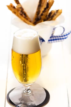 A glass of beer and spicy puff pretzel sticks in background on white wooden table