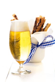 A glass of beer and spicy puff pretzel sticks in background on white wooden table