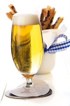 A glass of beer and spicy puff pretzel sticks in background on white wooden table