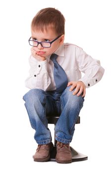 Serious clever kid in jeans and shirt sitting on small chair isolated on white background