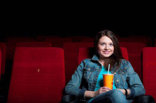 beautiful woman in a movie theater, watching a movie and drink a drink