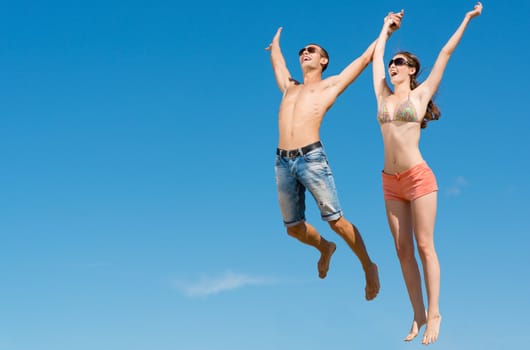 young couple jumping together on a blue sky background