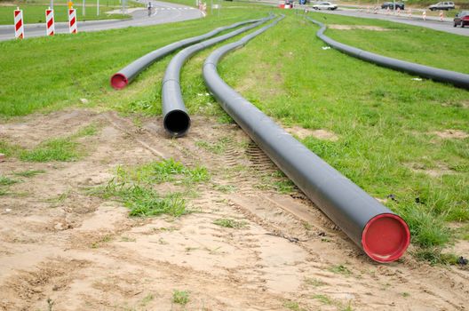 electricity cables wires with protective tube lay on green grassmeadow between road. communication construction industry.