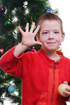 Young boy showing five fingers in front of christmas tree, looking at camera, vertical shot