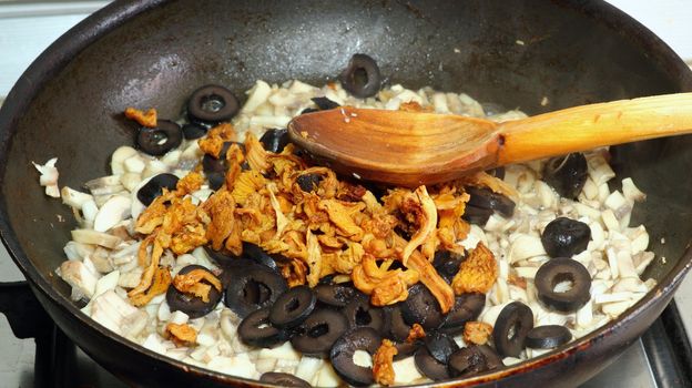 making pizza sauce with white and yellow mushrooms and black olives with a wooden spoon