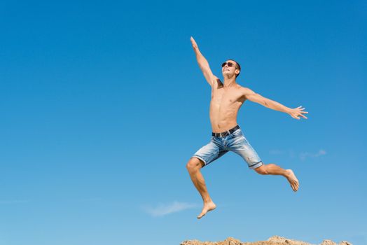 happy young man jumping on a background of blue sky, spreading his hands