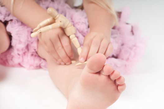 Foot and fingers of little girl and wooden toy in studio