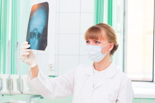 Young woman in protective mask dotstor looks at an X-ray of skull