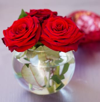 Round transparent vase with red roses on the table close-up