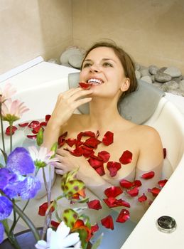 happy beautiful woman lies in bath with rose-petals