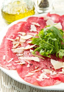 white dish with carpaccio of beef on arugula  