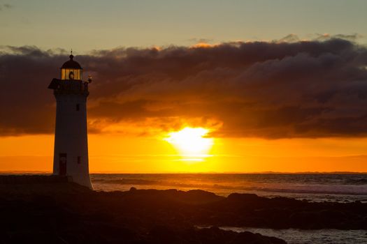 Port Fairy lighthouse beach with red glowing sunrise in background.