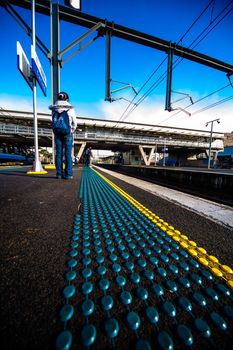 SYDNEY, AUSTRALIA - CIRCA JULY 2012: Unidentified woman stands and waits for the morning train at a platform with safety dots on clear sunny blue sky day circa July 2012 in Sydney, Australia.