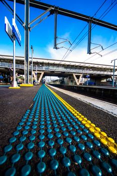 Urban train metro station with lower ground angle showing yellow and blue safety dots on clear blue sky day.