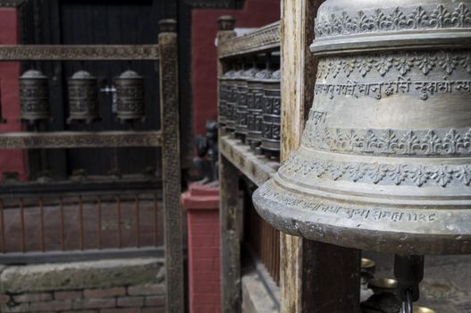 bell in foreground and prayer wheels in kathmandu, nepal