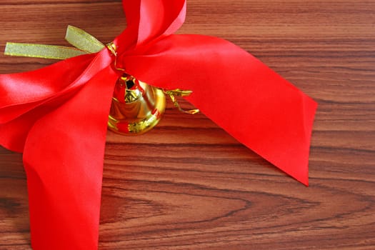 Bell with red ribbon over wooden background 
