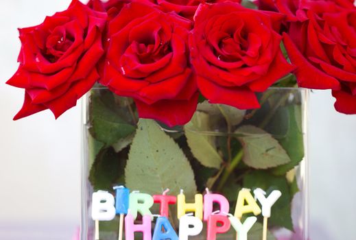 Candles of the letters "Happy birthday" in the background of a bouquet of red roses