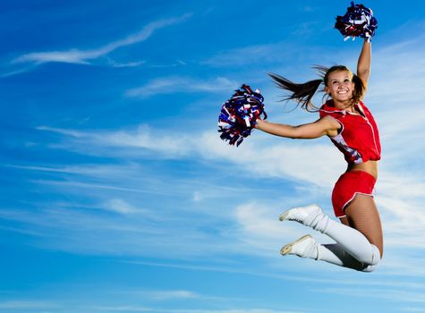 Young cheerleader in red costume jumping against blue sky