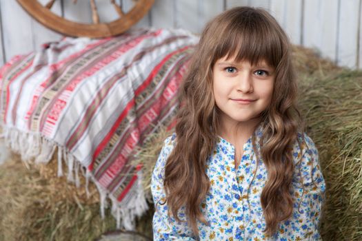 Portrait of friendly little blond girl villager in wooden hayloft with vintage decoration