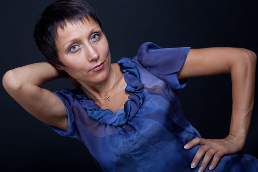 Half-length portrait of stylish young brunette woman in blue blouse on black background