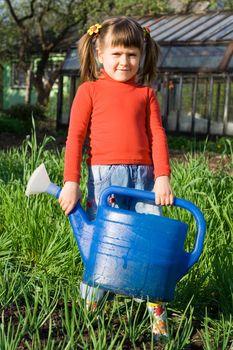 Little girl with watering can is standing on the vegetable garden near onion patch