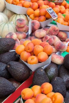 Plates with ripe orange apricot, fig peach, purple avocados, melons at fruit market