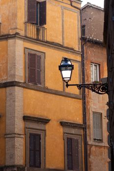 Picturesque facades of old medieval multistory urban residential stone brick-red houses with street lamp and icon on wall in city Rome Italy